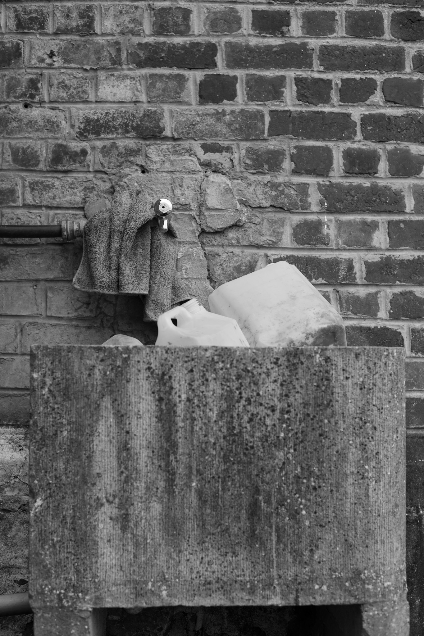 AdVitam_AMarly_Untitled16_2155 Français: Cette photo de bidons dans un évier en pierre fait partie de la série Ad Vitam. Ad Vitam est une série de photos réalisées par Alexandre Marly, photographe de portraits et de documentaires Belge. Photographie noir et blanc de bidons blancs, d'un évier en pierre et d'un robinet contre un mur de briques dans un cimetière. Technique: Nikon D850. English: This photo of cans in a stone sink is part of the Ad Vitam series. Ad Vitam is a series of photos made by Alexandre Marly, Belgian portrait and documentary photographer. Black and white photograph of white cans, a stone sink and a faucet against a brick wall in a cemetery. Technique: Nikon D850.